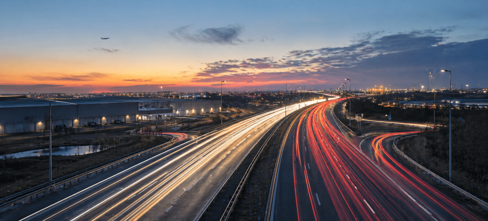 Long exposure of a highway at sunset with vibrant red and white light trails.